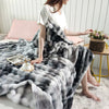 A woman is sitting on a white rug draped in a gray and white plush rabbit fur throw blanket.