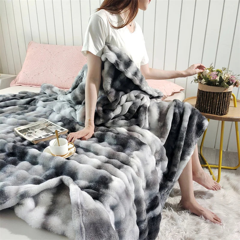 A woman is sitting on a white rug draped in a gray and white plush rabbit fur throw blanket.