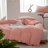 A pink minimalist duvet cover is spread on a bed with white bedding and natural light in the background.