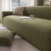 A textured olive green sofa slipcover with a neutral throw pillow and a book resting on the cushion.