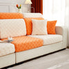 A beige sofa with orange and white patterned cushions and a matching ottoman on a light rug.