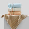A stack of three rolled face towels in light blue, cream, and peach colors with a beige towel draped below.