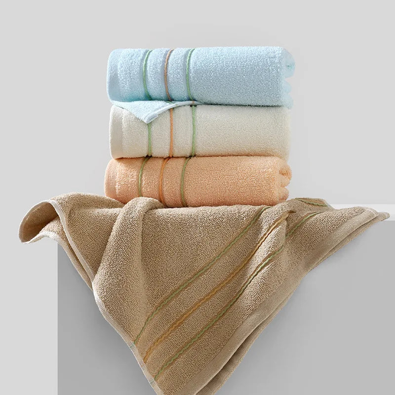 A stack of three rolled face towels in light blue, cream, and peach colors with a beige towel draped below.