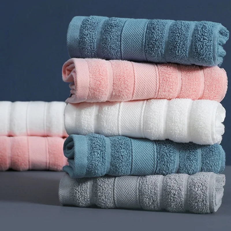 A stack of four rolled pure cotton face towels in shades of blue, pink, and white.
