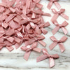 A collection of pink satin ribbon bows scattered on a white marble surface.