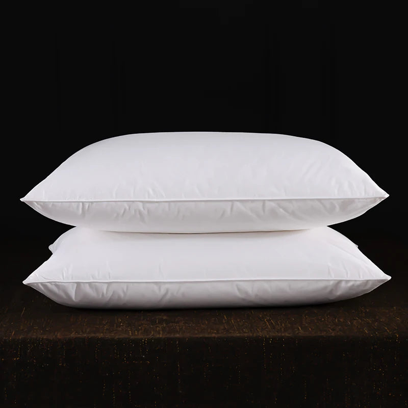 Two white natural goose down and feather sleeping pillows stacked on a dark surface.