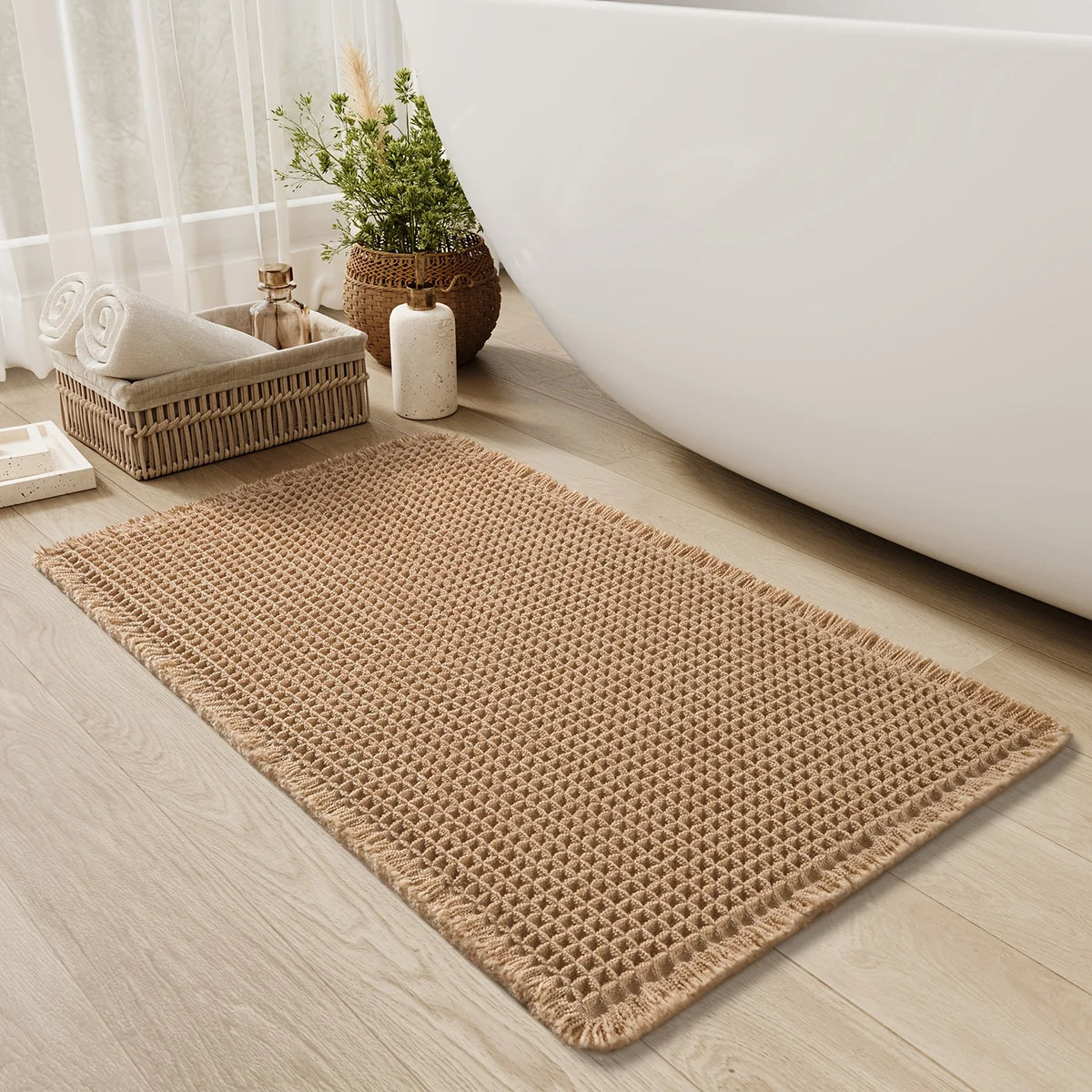 A beige waffle texture bath mat placed on a light wood floor next to a white bathtub.
