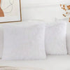 A set of two white faux fur throw pillows resting on a white sofa.