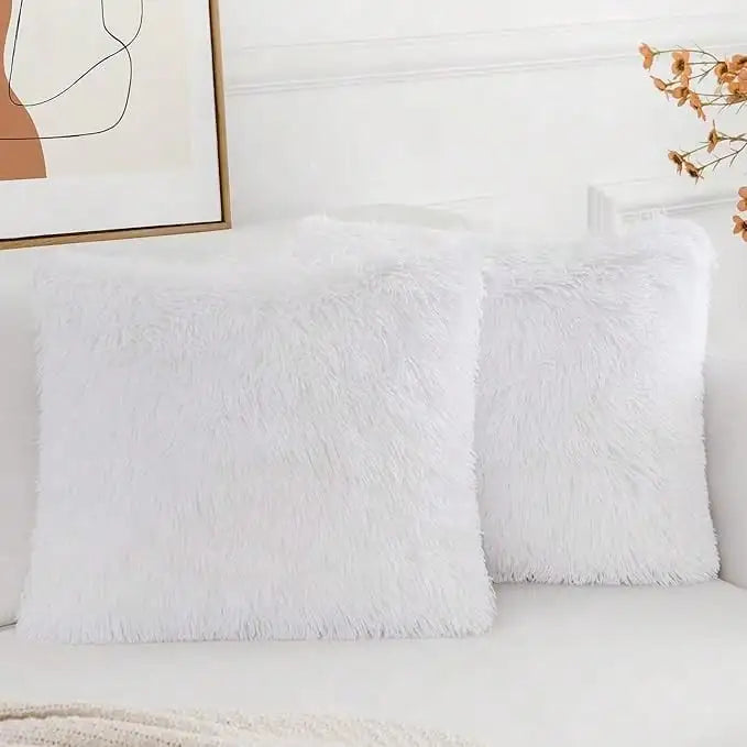 A set of two white faux fur throw pillows resting on a white sofa.