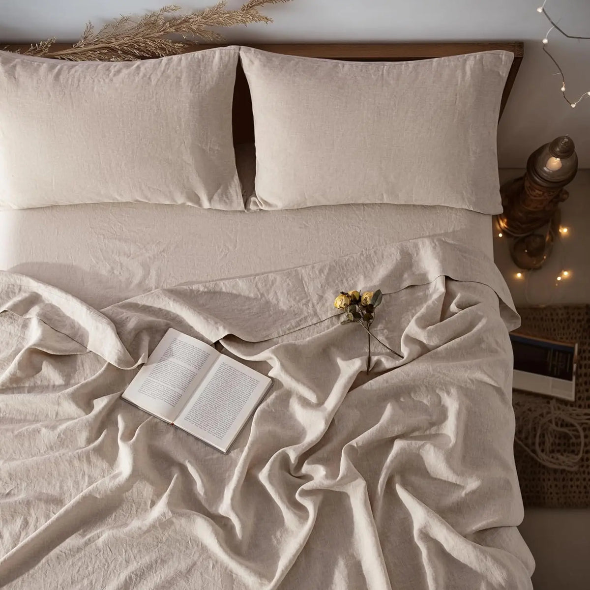 A beige French stone washed linen bedding set featuring three pillows and a draped sheet on a bed.