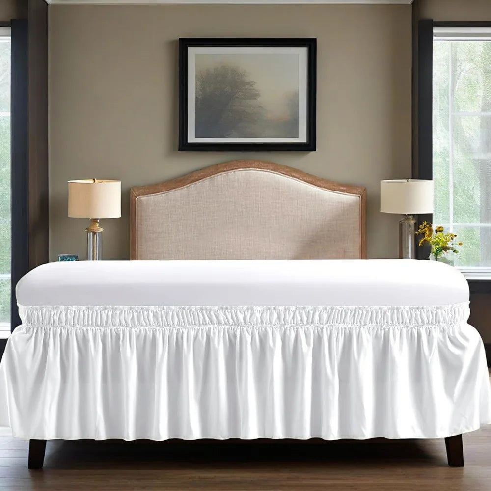 A white bed with a upholstered headboard and ruffled skirt set against a neutral wall.
