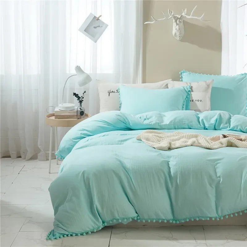 Light aqua duvet cover set with pom-pom decoration on a bed in a bright room.