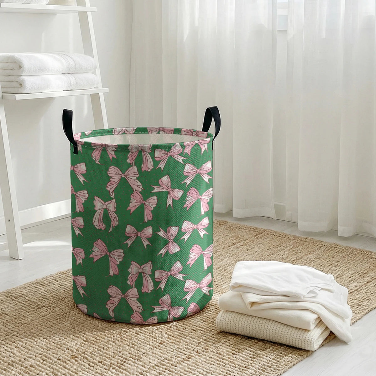 A green canvas laundry basket with pink bow patterns sitting on a woven mat next to a white shelf.