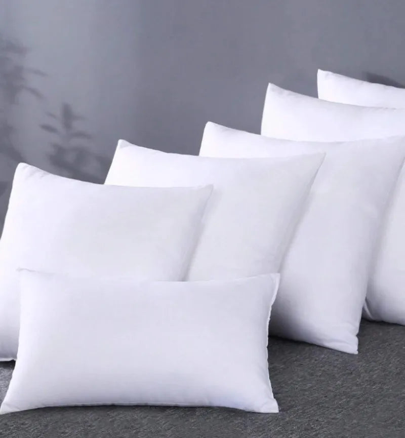 A stack of white polyester cushion inserts for throw pillows arranged on a gray surface.