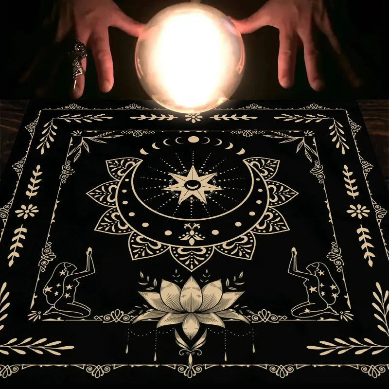 A hand holds a glowing orb above a dark mat decorated with celestial and floral tarot symbols.
