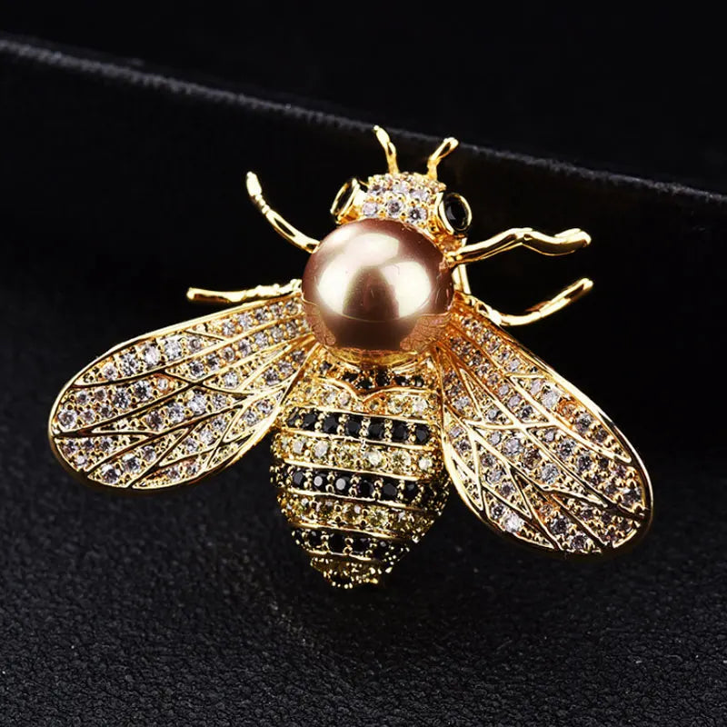 A gold-toned crystal bee brooch featuring a pearl accent and detailed diamond-like wings.