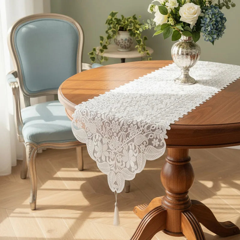 A round wooden dining table set with an embroidered white lace table runner and a light blue upholstered chair.