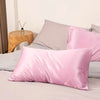 Pink satin pillowcases on a bed with gray and beige bedding.