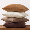 A set of four neutral corduroy throw pillow covers in varying shades of brown and beige stacked on a wooden surface.