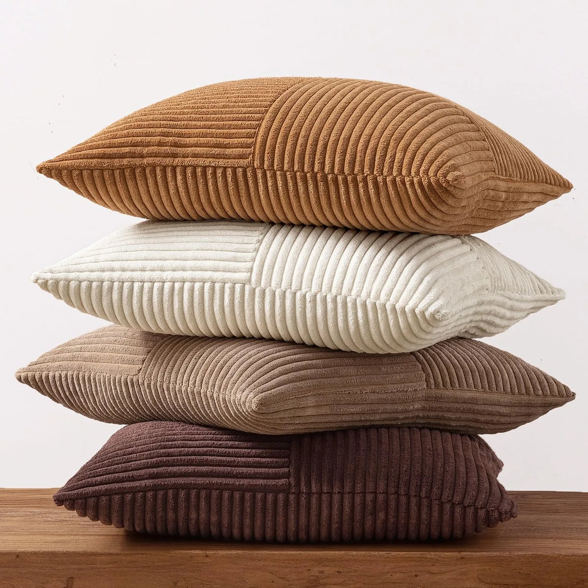 A set of four neutral corduroy throw pillow covers in varying shades of brown and beige stacked on a wooden surface.