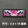 Black embroidered patch featuring pink and white stylized cat or feline eyes.