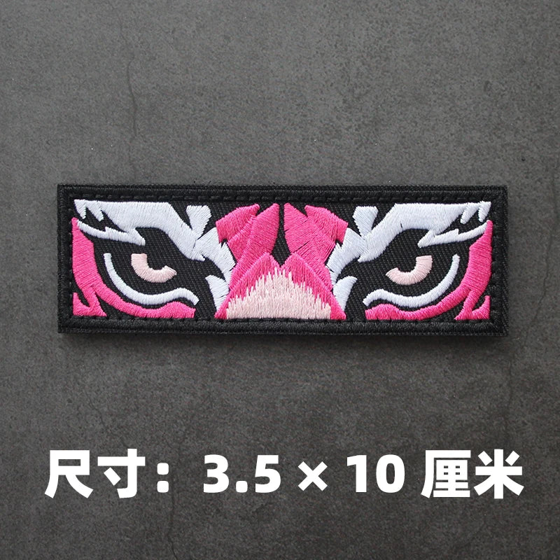 Black embroidered patch featuring pink and white stylized cat or feline eyes.