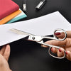 A hand holds professional stainless steel sewing scissors poised over a white sheet of paper.