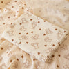 A soft double-layer cotton baby swaddle blanket with a subtle pattern lies on a light fabric background.