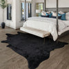 A modern faux animal skin rug in black with a non-slip backing placed on a light wood floor.