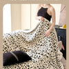 A woman is wrapped in a cream and black leopard print jacquard knit throw blanket on a dark surface.
