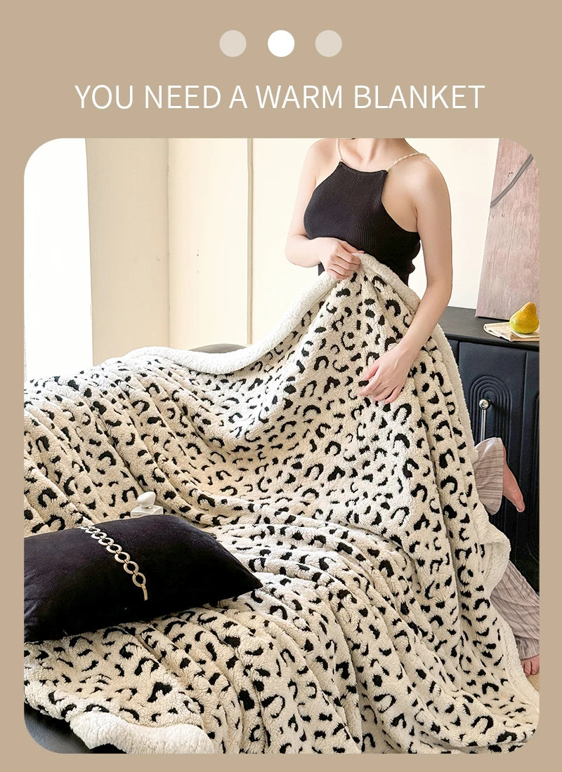 A woman is wrapped in a cream and black leopard print jacquard knit throw blanket on a dark surface.