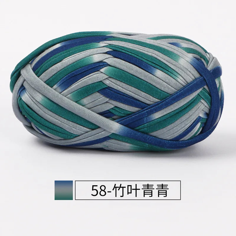 A ball of hand-dyed fabric strip yarn featuring shades of green, blue, and gray.