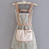 A floral pattern kitchen apron with adjustable straps and a pink pocket hanging on a wooden hanger.
