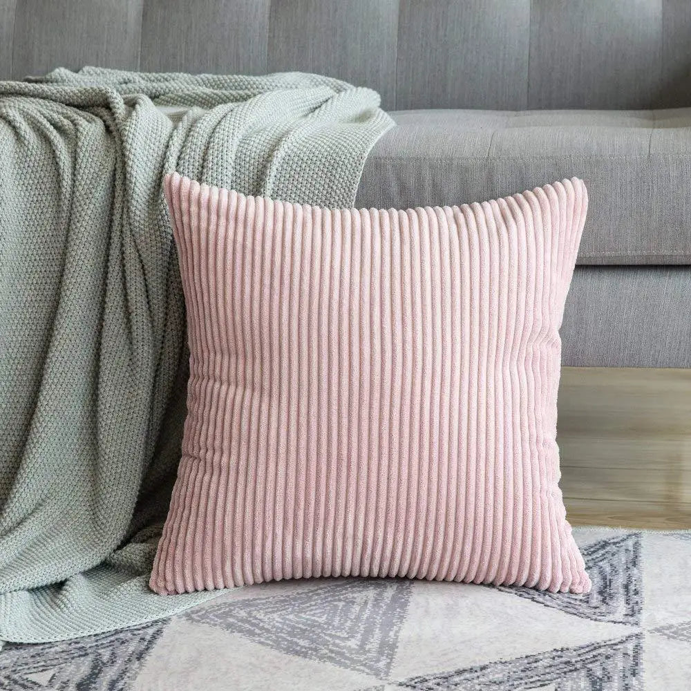 A pink ribbed throw pillow resting on a light gray sofa next to a green blanket.