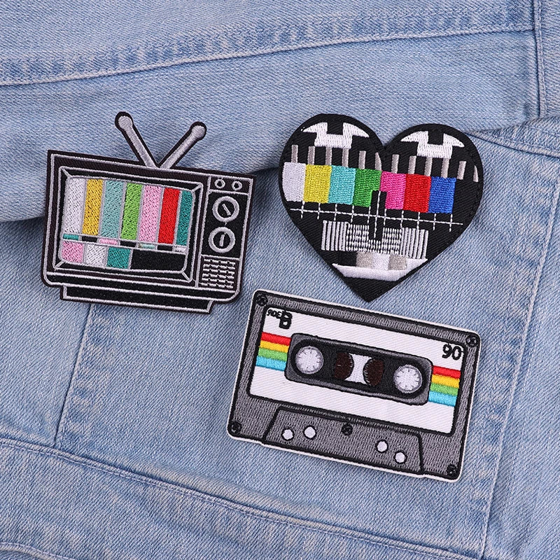 Three embroidered patches featuring a television, a heart, and a cassette tape design on a denim jacket.