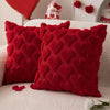 Two red heart-shaped textured plush cushions resting on a white sofa.