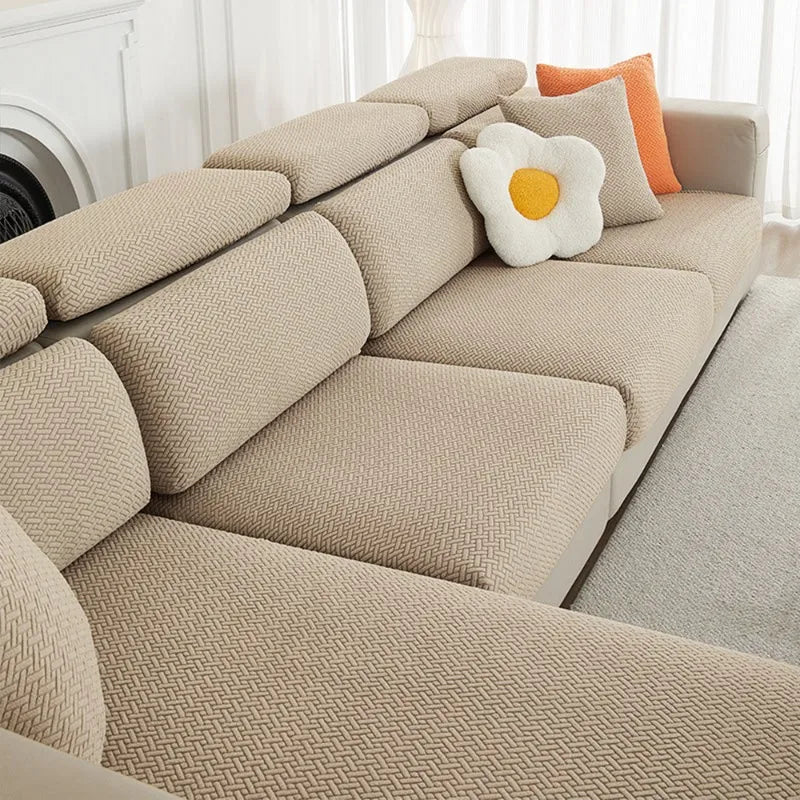 A beige jacquard elastic sofa cushion slipcover with an orange accent pillow on a light-colored sofa.