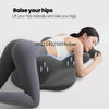 A woman is lying down, using a gray memory foam pillow to raise her hips and legs for back support.