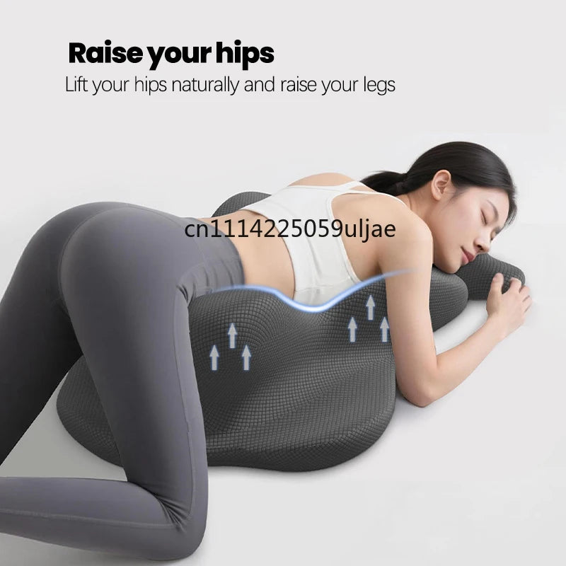 A woman is lying down, using a gray memory foam pillow to raise her hips and legs for back support.