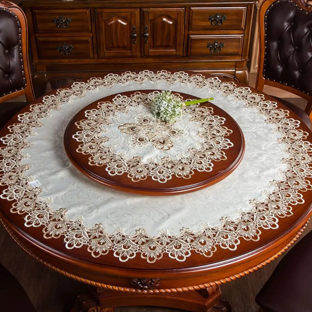 A round wooden table set with a lace-trimmed tablecloth and dark leather chairs.
