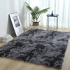 A thick gray faux fur area rug placed on a light wood floor in a bright room with a potted plant and a small table.