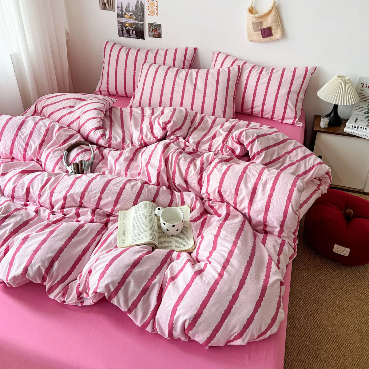 A pink duvet cover set with white stripes and matching pillowcases is displayed on a bed.