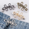 A collection of adjustable leaf clover waist tighteners in silver and gold tones displayed on a denim fabric.