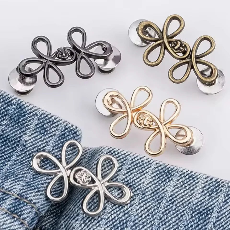 A collection of adjustable leaf clover waist tighteners in silver and gold tones displayed on a denim fabric.