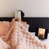 A person is relaxing in bed covered by a pink faux rabbit fur throw blanket while reading books.