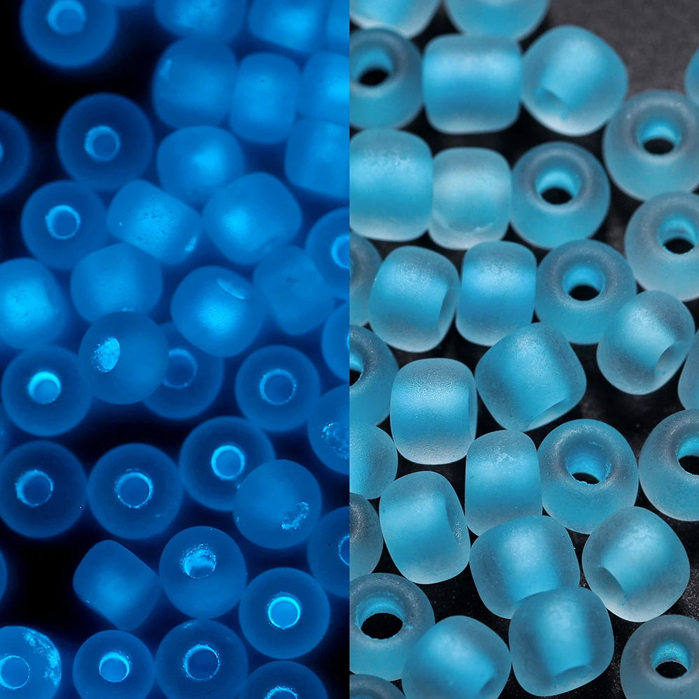 A close-up view of small, translucent blue glass seed beads with a glow-in-the-dark effect.
