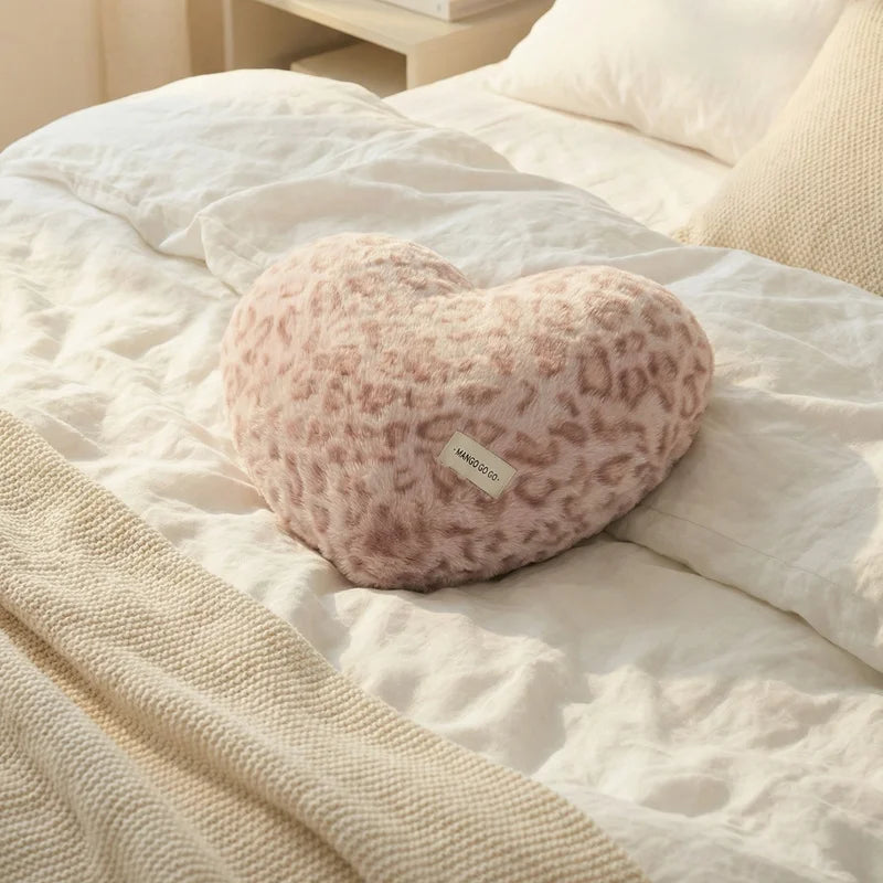 A pink leopard print plush heart-shaped pillow resting on white bedding.