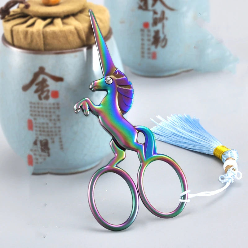 A pair of iridescent, three-color stainless steel unicorn sewing scissors resting on a white surface.