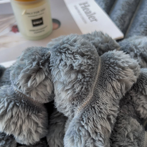 A close-up of a thick, gray, fuzzy blanket being held, with a white label in the background.