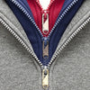 Close-up of a gray garment featuring a red and navy zipper with gold pull replacements.